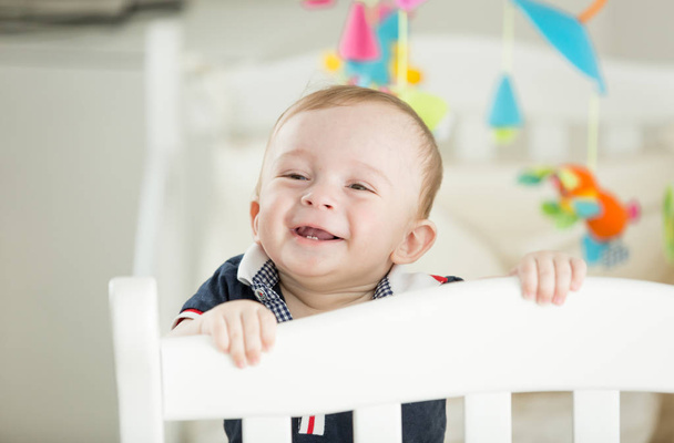 Portrait of happy smiling baby boy with 2 teeth standing in crib - 写真・画像
