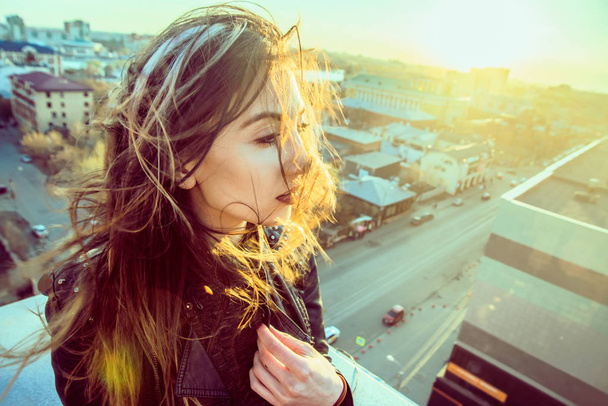 Beautiful girl sitting on the rooftop watching sunset over the city - Photo, Image