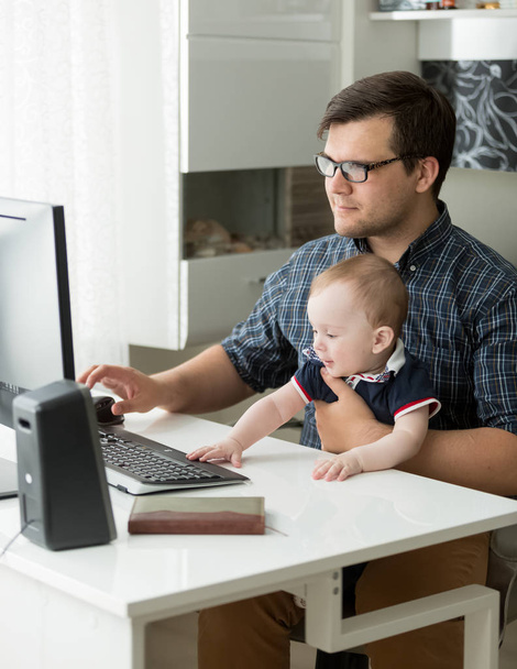 Portrait of young man working at office and holding his 1 year old baby son - Photo, Image