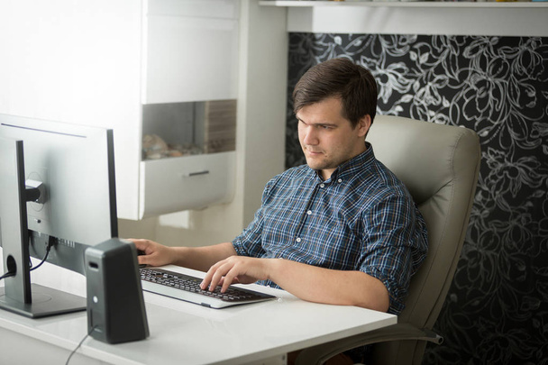Portret młodego self-emlployed człowieka w checkeered koszuli siedzi w home office i działa na komputerze - Zdjęcie, obraz