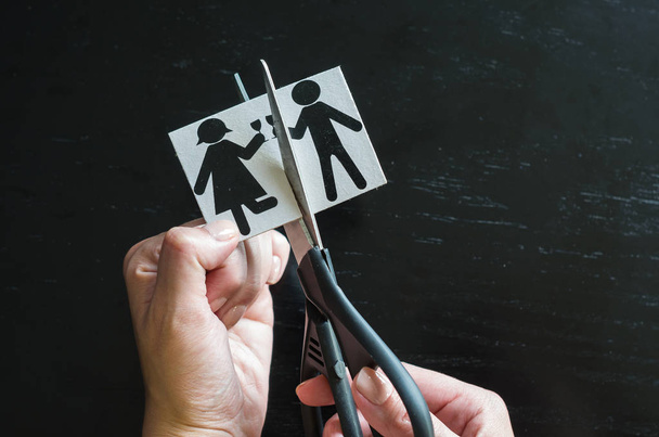 Family divorce. Cropped image of hand cutting paper family with scissors over wooden table. - Photo, Image