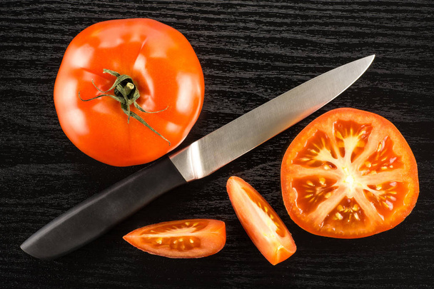 Red tomato composition with a knife isolated on black wood background top view one whole one section half and two slice - Foto, Bild