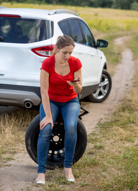 Giovane donna con auto rotta sittign sulla ruota di scorta e chiamando il servizio auto per aiuto
 - Foto, immagini