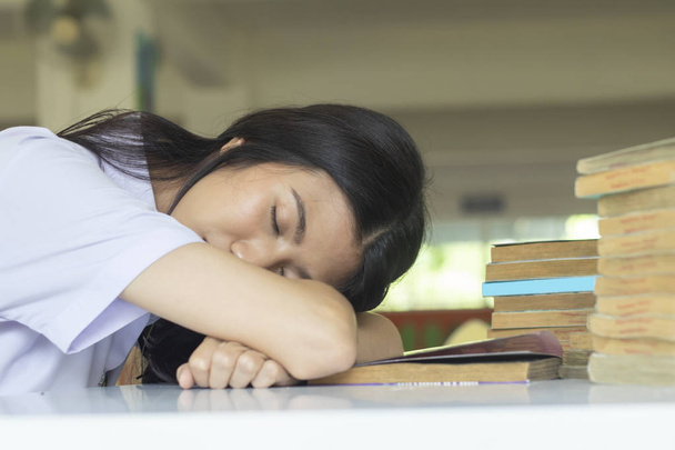 Väsynyt nukkuva tyttö opiskelija opiskelee kirjaston pöydässä
 - Valokuva, kuva