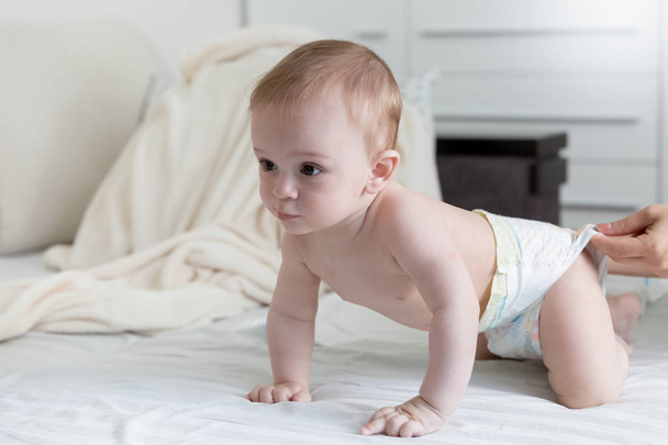 Cute 9 months old baby boy in diapers crawling on bed - Photo, Image
