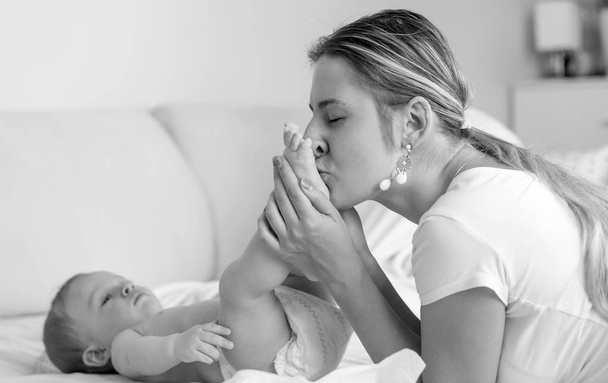 Portrait noir et blanc de jeune mère embrassant ses pieds de fils de bébé
 - Photo, image