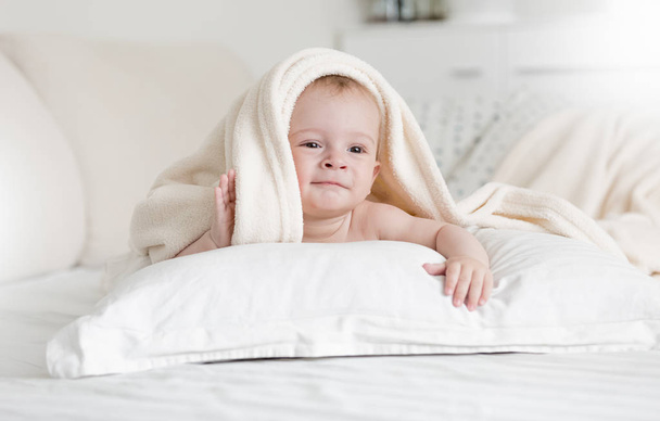 Retrato de adorable niño de 9 meses acostado en la cama bajo una gran manta suave
 - Foto, imagen