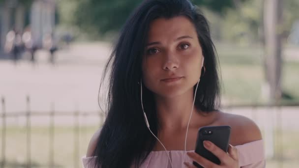 Close up shot of young woman listening music in the headphone while using smartphone in the city. Portrait shot - Materiał filmowy, wideo