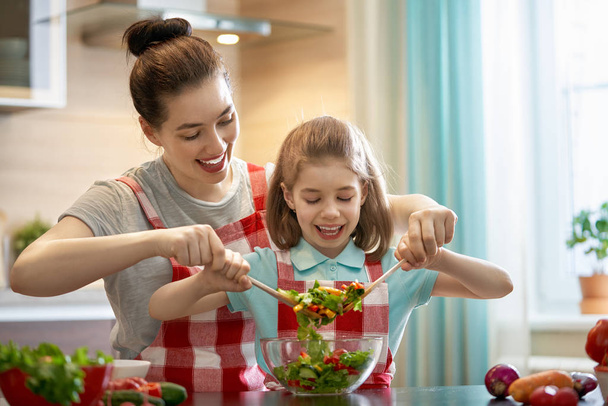 Healthy food at home. Happy family in the kitchen. Mother and child daughter are preparing the vegetables. - Photo, Image