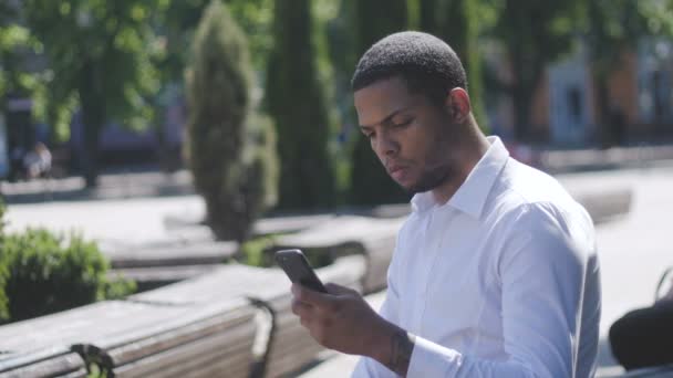 African American Man sms γραπτών μηνυμάτων χρησιμοποιώντας εφαρμογή στο έξυπνο τηλέφωνο στην πόλη. - Πλάνα, βίντεο