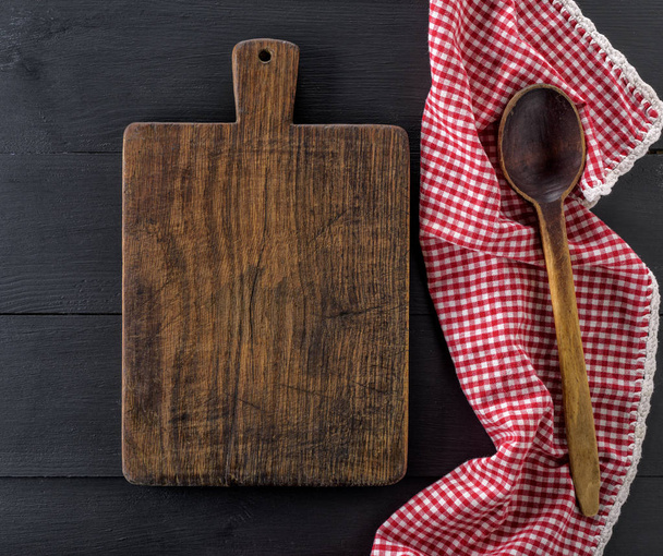 empty old wooden cutting board and a wooden spoon on a black table, top view - Fotoğraf, Görsel