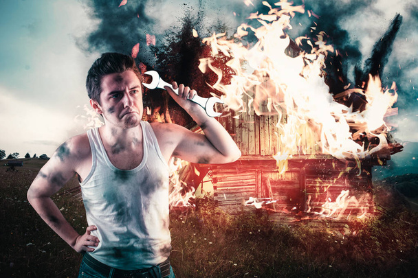 Angry man holding a wrench with his house on fire in the background. Home insurance concept - Photo, Image