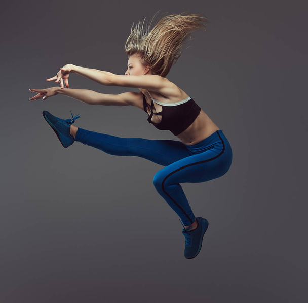 Jovem bailarina em danças de sportswear e salta em um estúdio. Isolado em um fundo cinza
. - Foto, Imagem