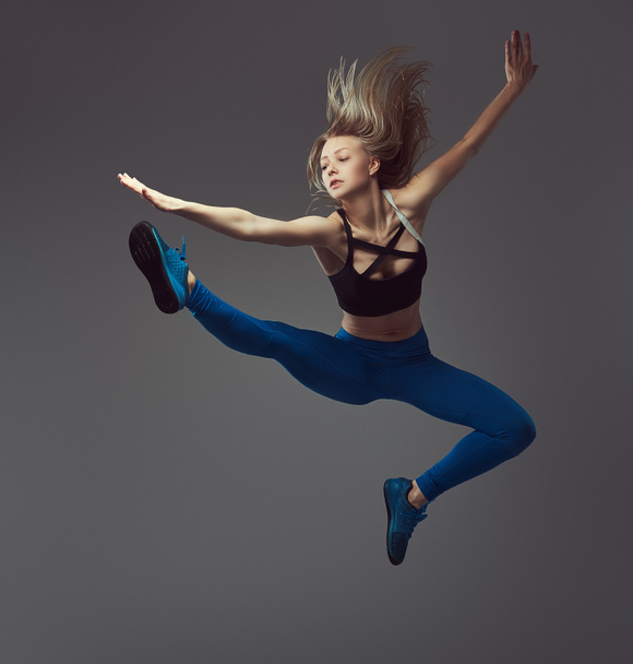Young ballerina in sportswear dances and jumps in a studio. Isolated on a gray background. - Fotó, kép