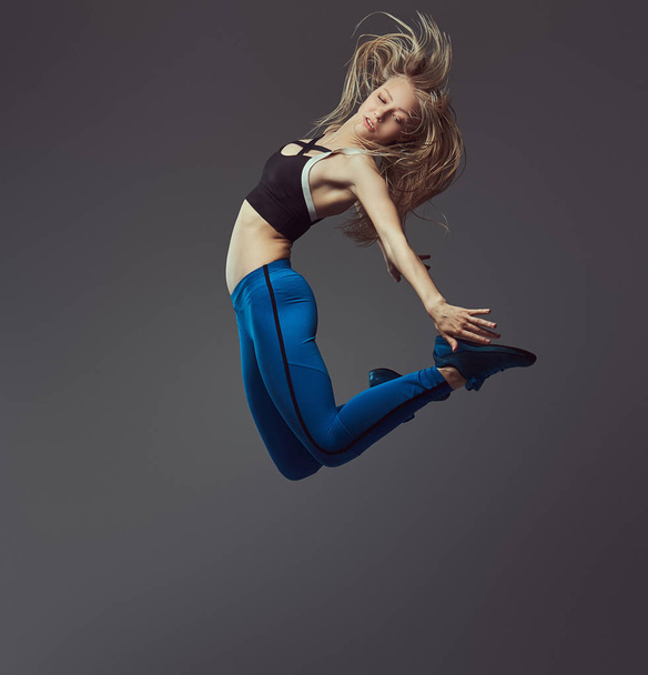 Молода балерина в спортивному одязі танцює і стрибає в студії. Ізольовані на сірому фоні
. - Фото, зображення