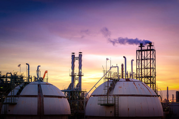 Fabrieksinstallatie op zonsondergang hemelachtergrond, Gas bol opslagtank in petrochemische plant met rook stapels op moment van de avond - Foto, afbeelding