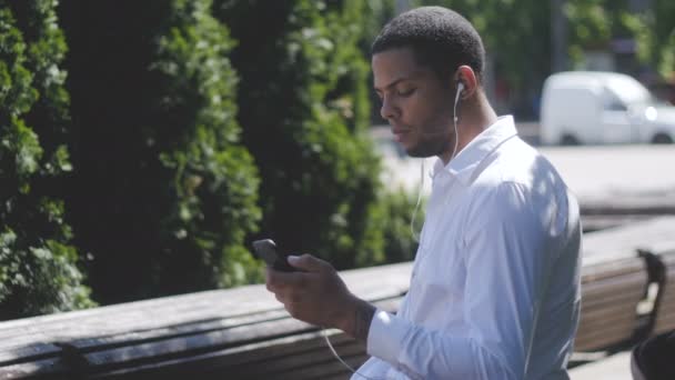 African American Man sms γραπτών μηνυμάτων χρησιμοποιώντας εφαρμογή στο έξυπνο τηλέφωνο στην πόλη. - Πλάνα, βίντεο