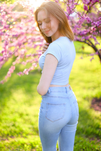 Uroczy dziewczyna ubrana w dżinsy, stojąc w promienie słońca z kwitnące gałęzie tło. - Zdjęcie, obraz