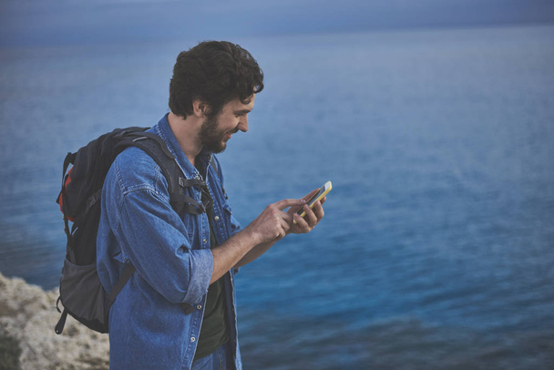 Excited guy using smartphone near the sea - Foto, afbeelding