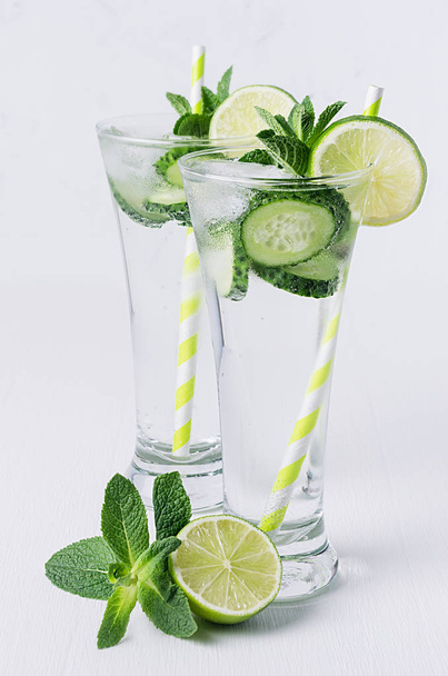 Cold mineral water with cucumber, lime, mint and ice on soft white background.  Summer refreshing drinks. - Foto, imagen