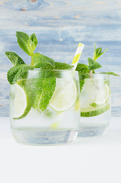 Mojito in two glasses with mint, slices lime, ice cubes, straw on soft shabby blue background, closeup. - 写真・画像