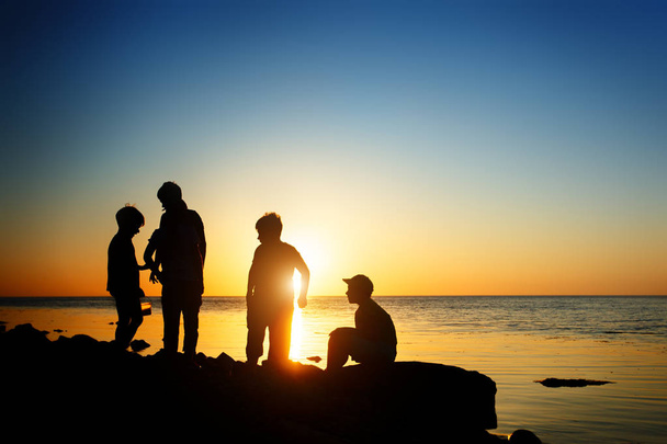 Children on the beach, fishing. Sunset shot, rear view. Sea background. - Фото, зображення