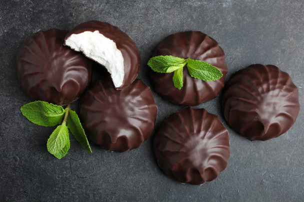 White marshmallow in chocolate and a mint leaf on a black background. Top view. - Photo, Image
