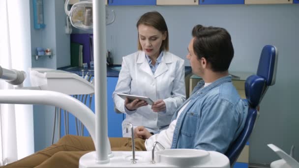 Dentist showing male patient x-ray on tablet - Materiał filmowy, wideo