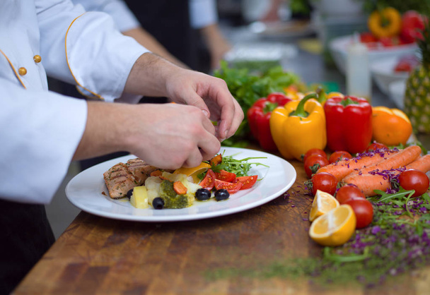 cook chef decorating garnishing prepared meal dish on the plate in restaurant commercial kitchen - Foto, Bild