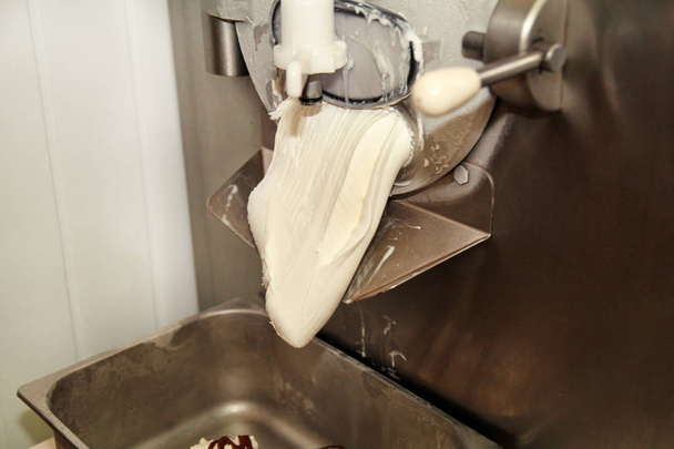 La máquina para hacer helados produce helado de vainilla con aderezo de chocolate y cae en un recipiente de acero. Preparación industrial de helado cremoso. Postres, dulces
. - Foto, Imagen