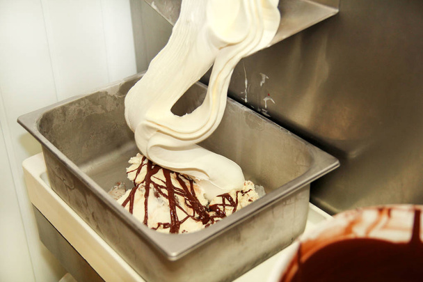 Machine de fabrication de crème glacée produit de la crème glacée vanille avec vinaigrette au chocolat et il tombe dans un récipient en acier. Préparation industrielle de crème glacée crémeuse. Dessert, bonbons
. - Photo, image