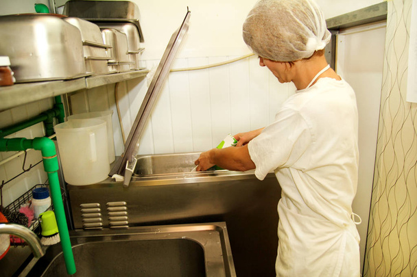 Female chef and worker is working at ice cream factory is pouring pasteurized milk and cooking mixing milk in pasteurization machine preparing basis for ice cream production. Preparation of ice cream. - Photo, Image