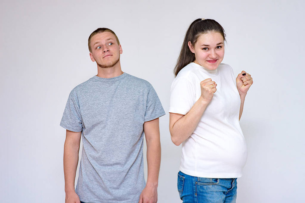 family relationships. Portrait of young married couple: husband and pregnant wife communicate in studio on white background. They stand directly in front of the camera and show different emotions - Φωτογραφία, εικόνα