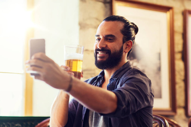 man with smartphone drinking beer at bar or pub - Foto, imagen
