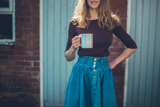 A young woman with a big mug of coffee is standing in the courtyard - Foto, Imagem