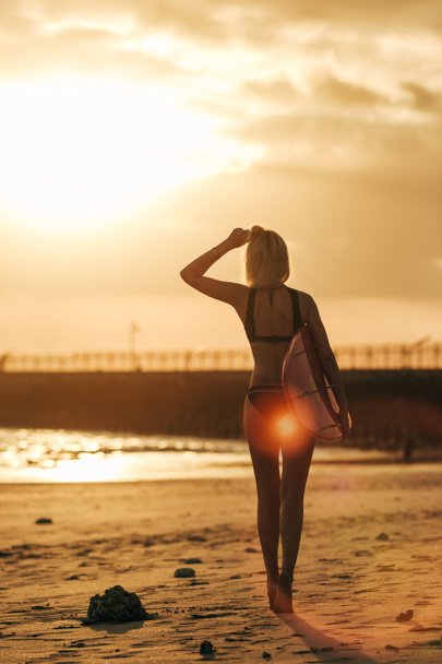 back view of girl posing with surfboard on beach at sunset with back light - Foto, Imagen