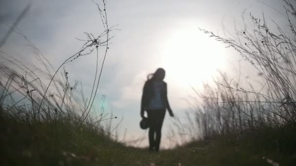 Νεαρή γυναικεία σιλουέτα περπάτημα στο πεδίο κατά το ηλιοβασίλεμα - Πλάνα, βίντεο