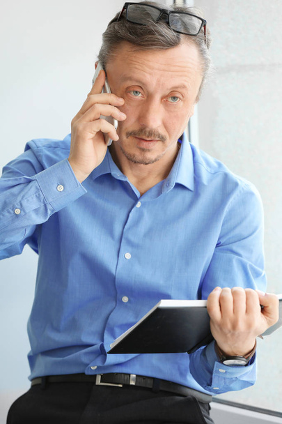 Mature man talking on mobile phone while working indoors - Foto, Imagen
