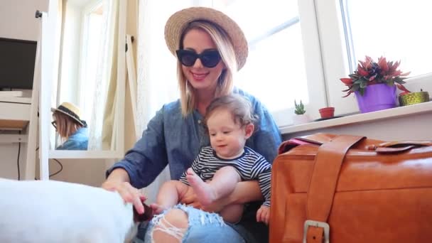 Woman in denim wear and hat sitting on floor, holding son in hands son and stroking dog - Footage, Video