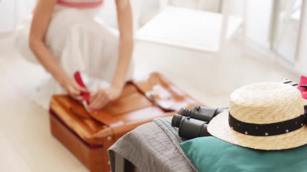 Vista superior de la mujer rubia en sombrero y vestido blanco sentado en el suelo y embalaje de ropa en la bolsa de viaje
 - Metraje, vídeo