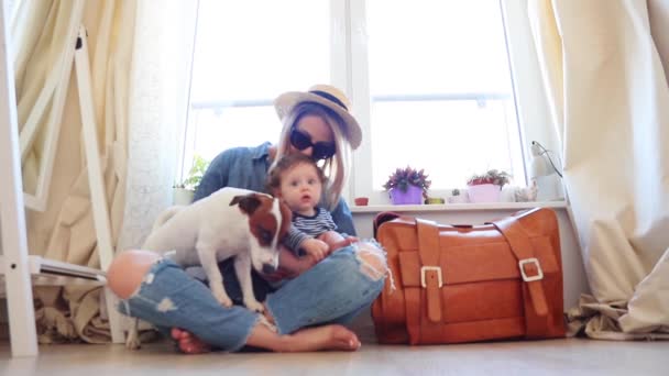 Woman in denim wear and hat sitting on floor, holding son in hands son and stroking dog - Footage, Video