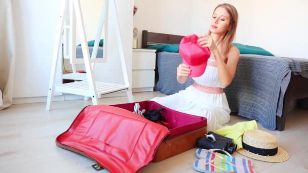 Aantrekkelijke blonde vrouw zittend op de vloer en verpakking van kleren in reistas - Video
