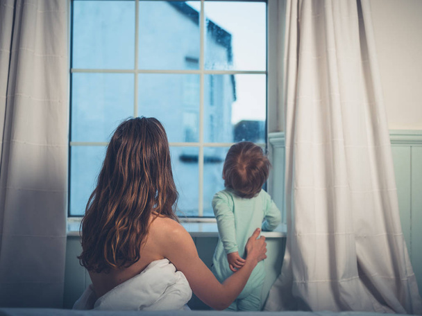 A young mother and her little boy are sitting in bed and looking out the window in the morning - Photo, Image
