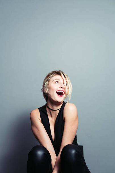 Gros plan portrait d'une jolie femme blonde, riant et regardant vers le côté, sur fond de studio uni
 - Photo, image