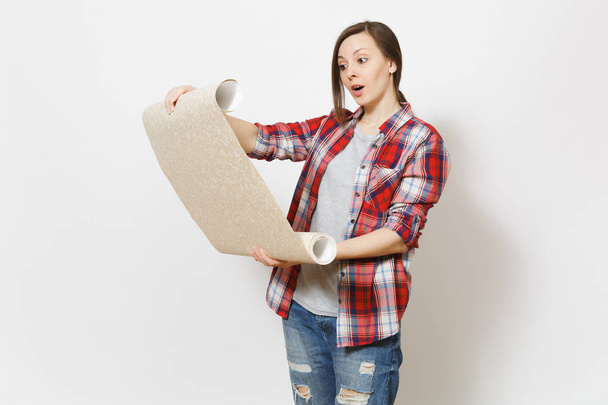Young concerned beautiful woman in casual clothes holding unrolled wallpaper roll isolated on white background. Instruments, accessories, tools for renovation apartment room. Repair home concept - Photo, Image