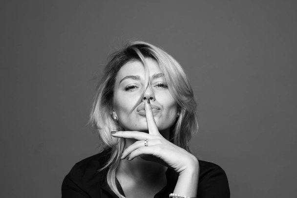 Portret van een jonge vrouw, die hand in de buurt van gezicht, vinger op de lippen, tegen een gewone studio close-up - Foto, afbeelding