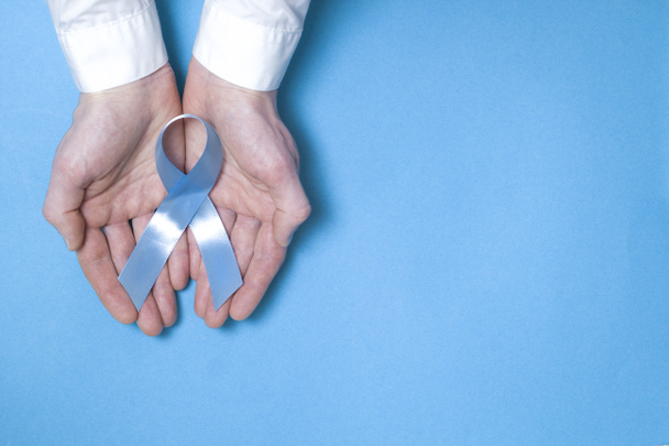 Символом мужчин, пострадавших от рака предстательной железы, является светло-голубая лента. Запись в руках человека на синем фоне. Копирование пространства
. - Фото, изображение