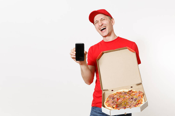Livraison homme souriant en uniforme rouge isolé sur fond blanc. Courrier homme pizzaman en bonnet, t-shirt tenant téléphone portable avec écran vide vierge, pizza italienne en carton plat. Espace de copie
 - Photo, image