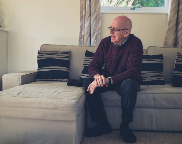 A senior man is sitting on a sofa indoors - Foto, afbeelding