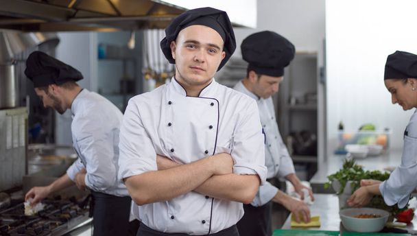 Portrait of young chef standing in commercial kitchen at restaurant - 写真・画像